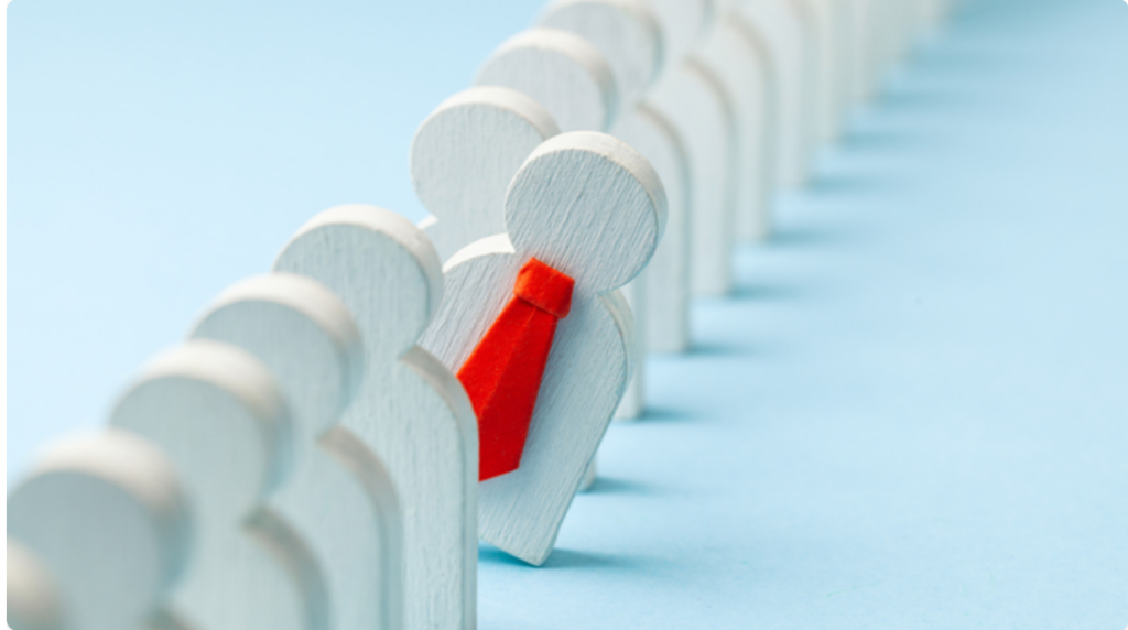 wooden men in line with one out of line in a red tie